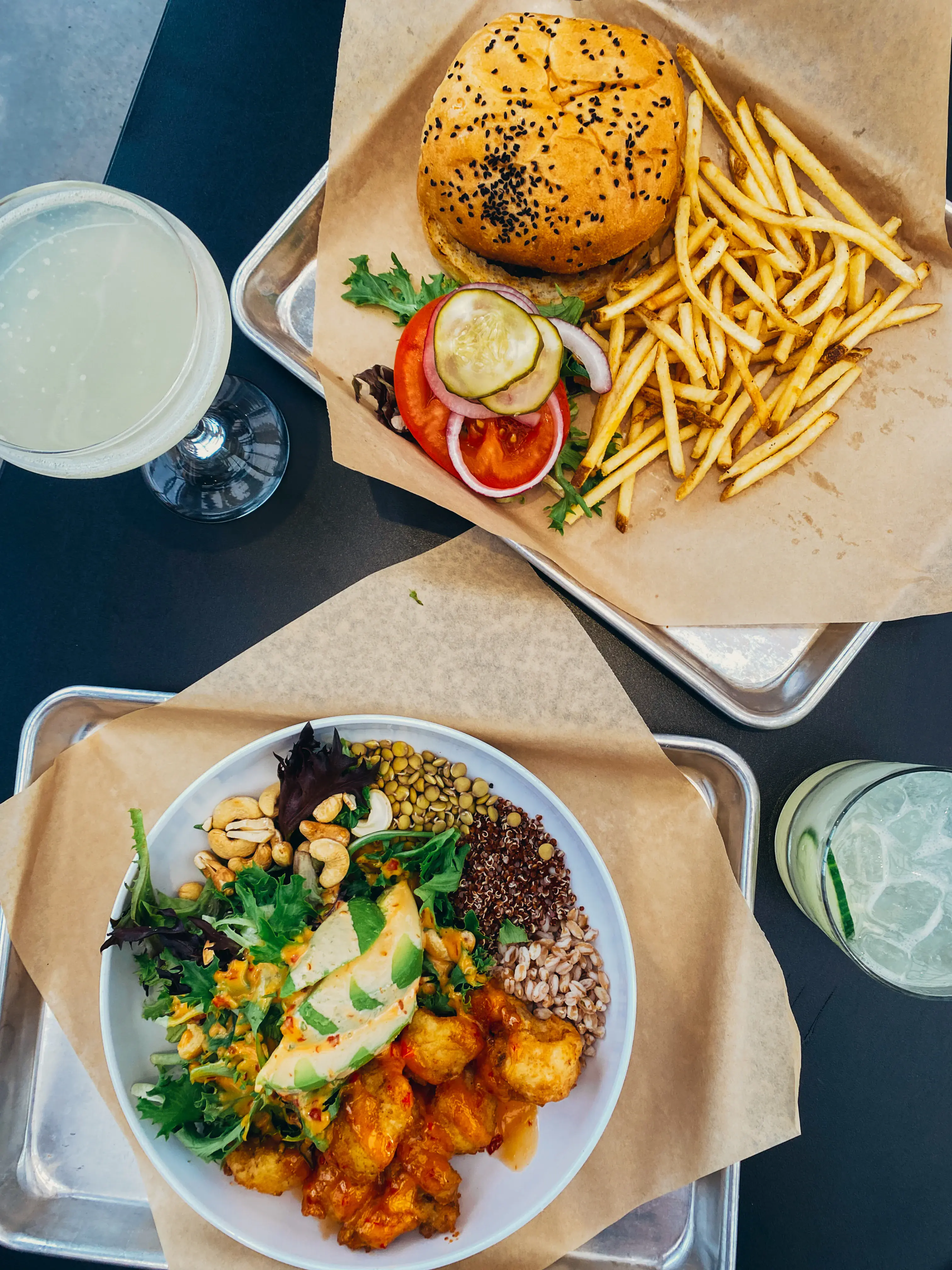 A top-down view of a meal consisting of a burger, fries, and a salad, with two glasses of drinks on the side.
